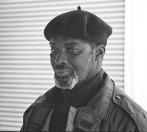 Photo of dark skinned man with gray beard in beret focusing intently to the left