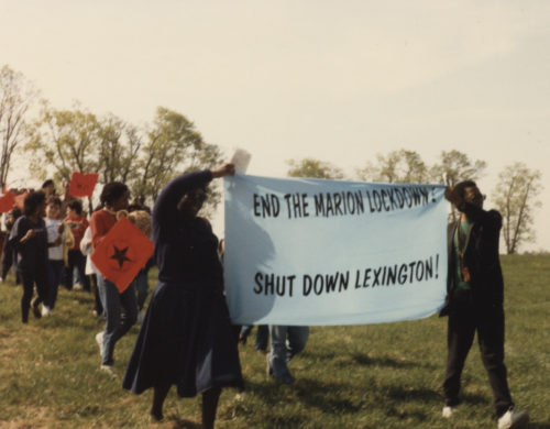 Demonstrators on grassy field holding banner END THE MARION LOCKDOWN! SHUT DOWN LEXINGTON!