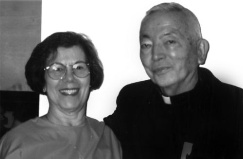 Photo of Puerto Rican mother with short hair and glasses smiling with Japanese American elder looking seriously at the camera