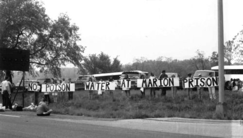 Protestors holding billboard type sign at side of road