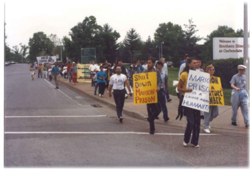 Scores of people marching along the side of a road with protest signs